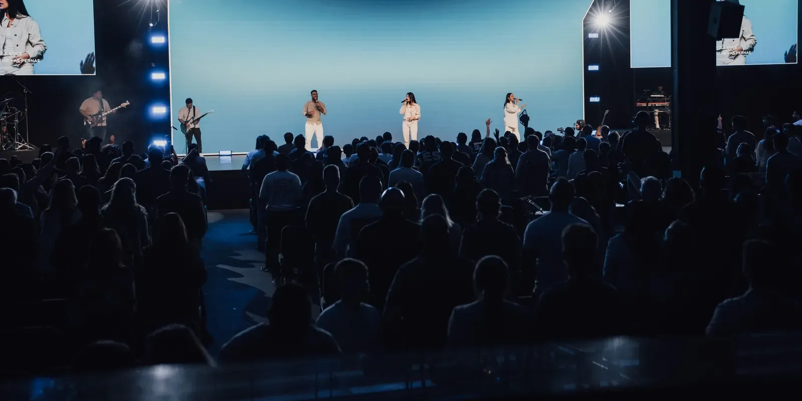 Igreja reunida em culto, vista do fundo do auditório, com a banda no palco